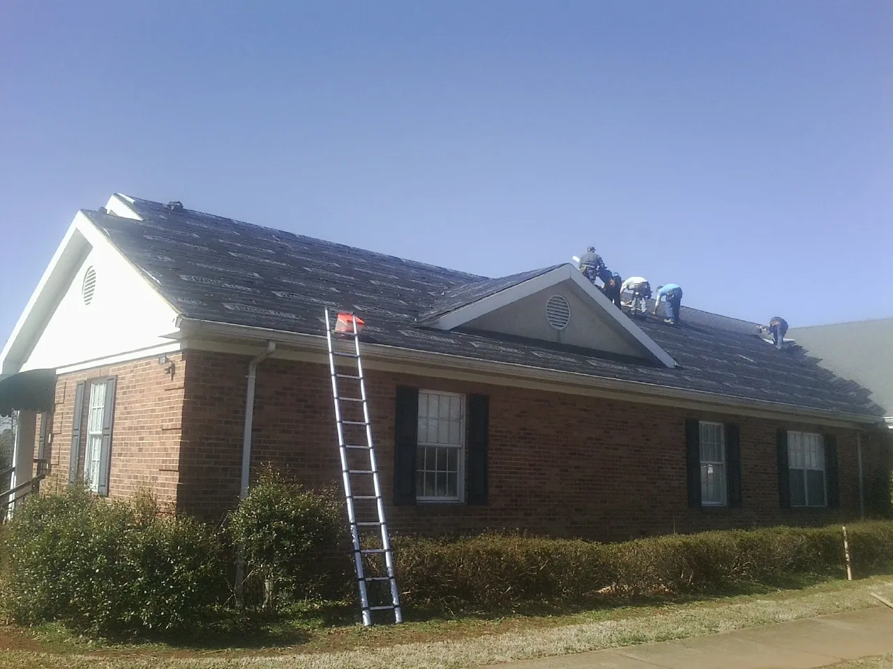 Crew tearing shingles off a brick ranch roof with a ladder set — Metal Roof Repair work by our crew in Callaway