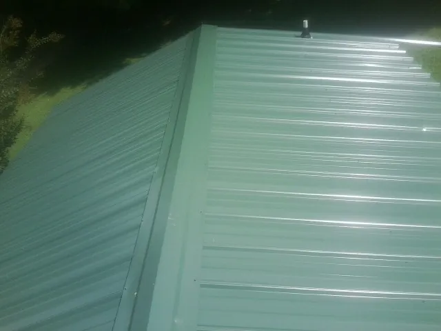 New green metal panels meeting at the ridge of a roof — Flat Roof Repair work by our crew in Callaway