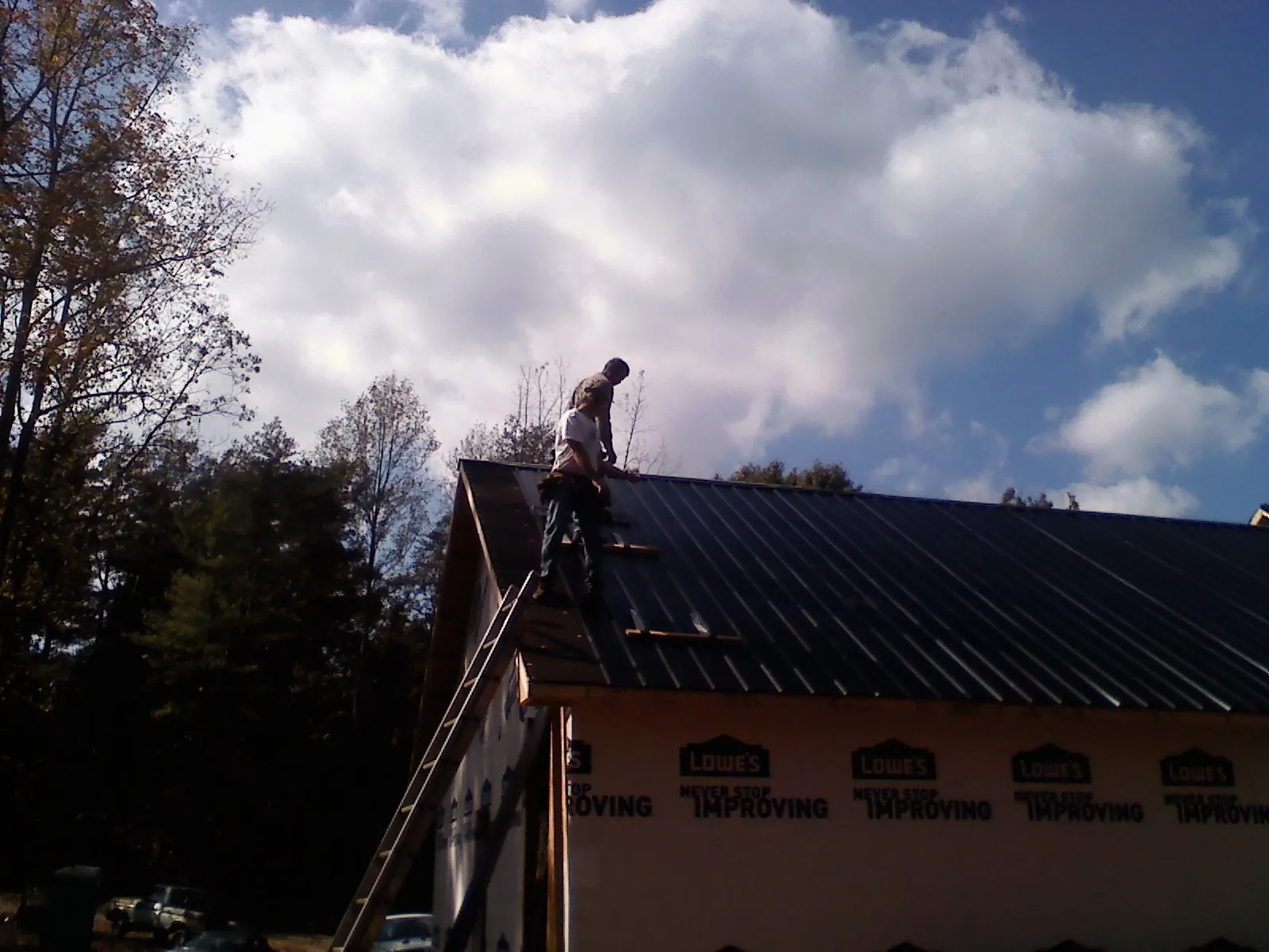 Roofer fastening dark metal panels high against a cloudy sky, from a Roof Inspection job in Callaway